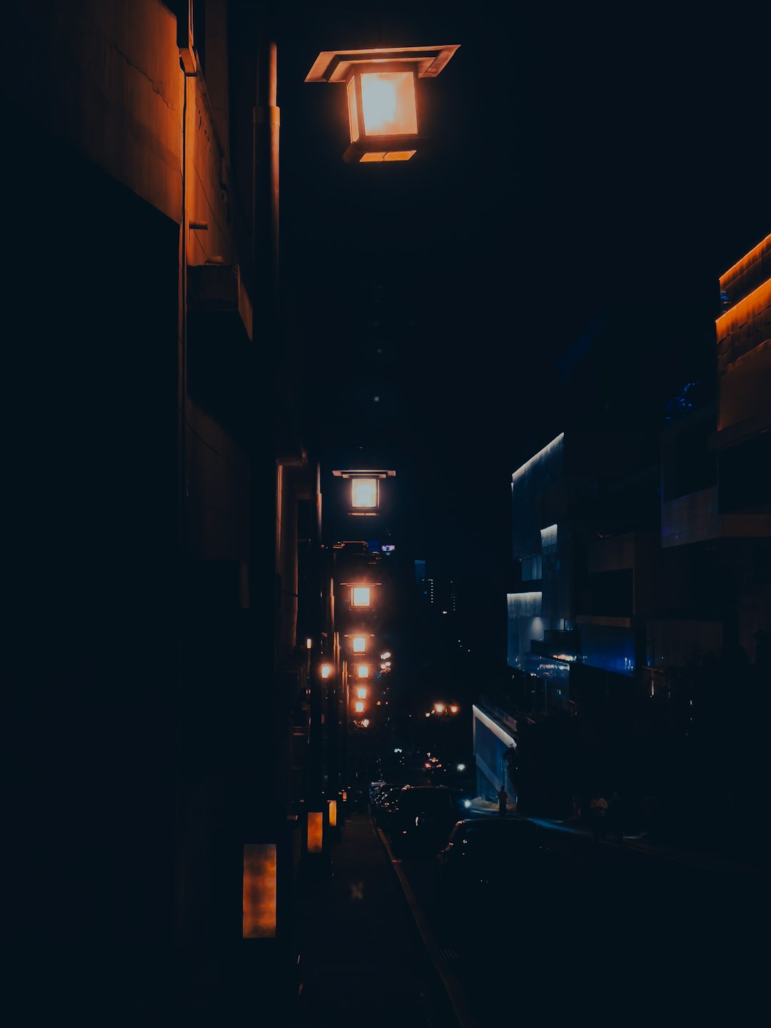 Empty city alleyway illuminated by glowing orange square streetlights.
