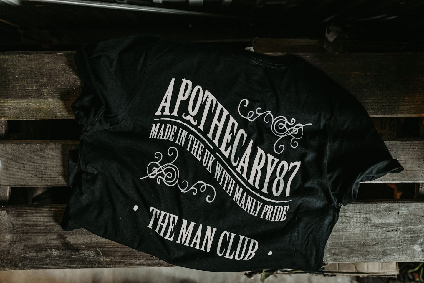 Black t-shirt with white vintage design resting on wooden pallet.