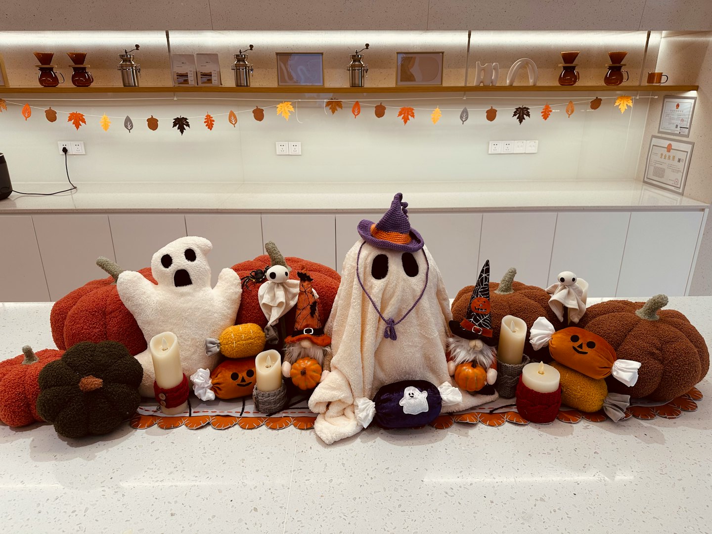 Plush ghost figures, pumpkin pillows, and witch gnomes on a table.