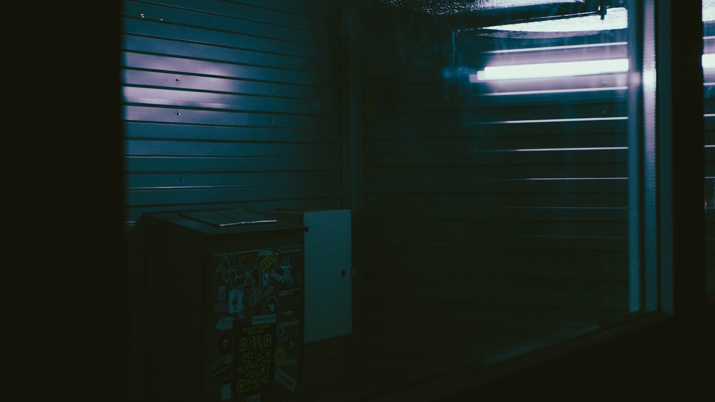 Sticker covered cabinet sits against a corrugated metal wall.
