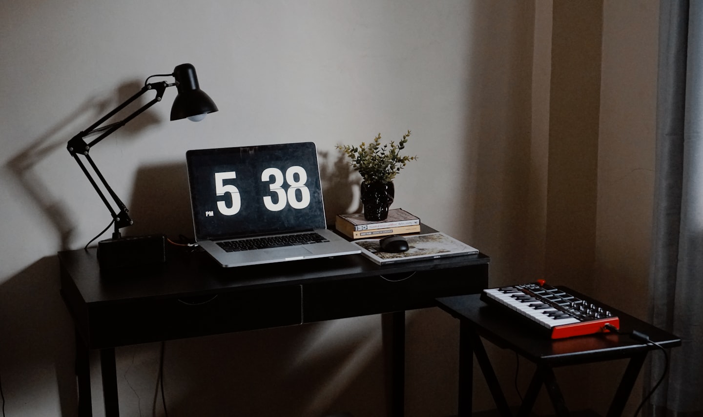 Laptop with digital clock and skull vase on office desk.